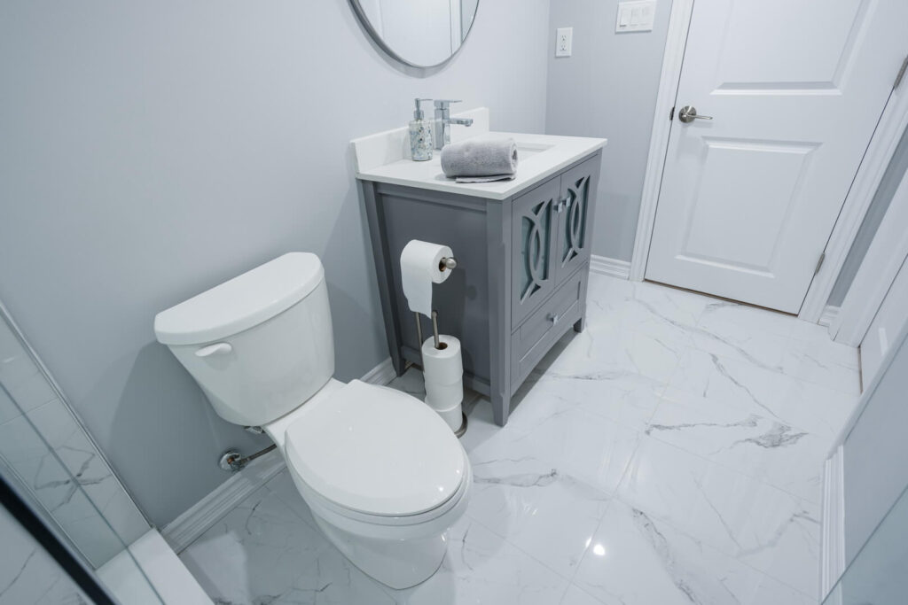 white tall tank toilet seat with marble flooring with vanity