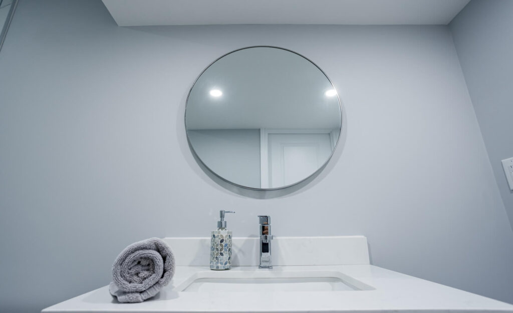 round bathroom mirror with white ceramic countertop and tap