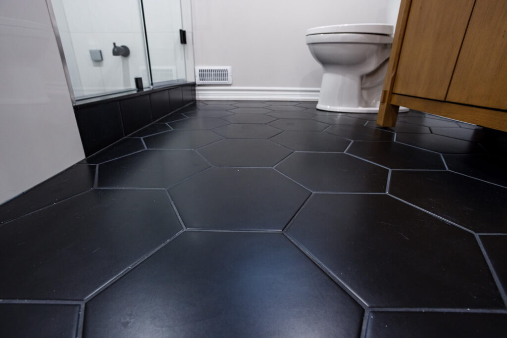 matt finish black hexagon tile flooring in bathroom with white toilet and wooden vanity