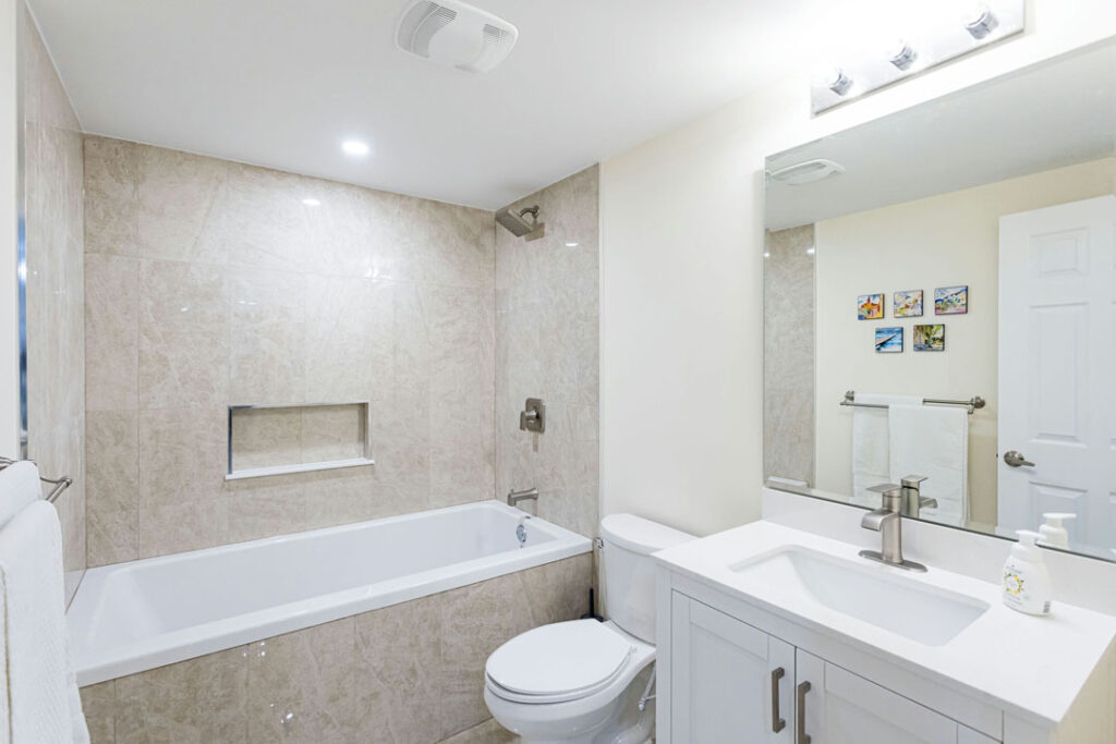 modern marble tiled bathroom wall with attached bathtub and vanity with toilet seat