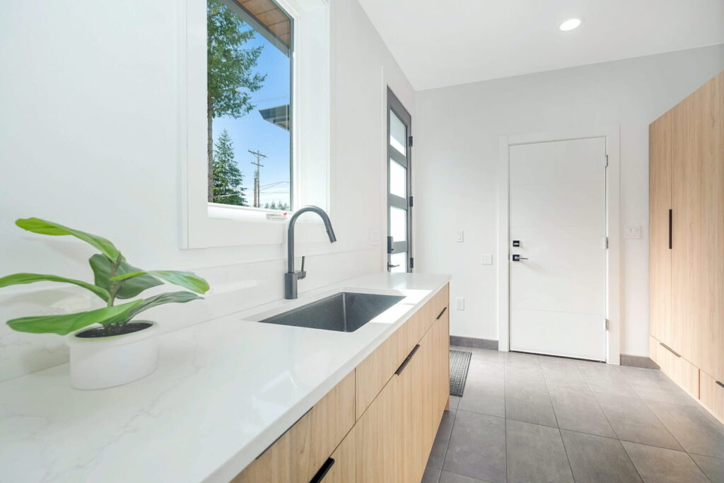 Contemporary laundry room remodel with minimalist cabinetry and functional layout Minimalist laundry room remodel with light wood cabinetry, large sink, and exterior door access