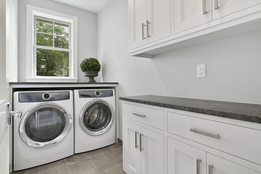 Modern laundry room renovation with custom cabinetry and front-loading appliances Laundry room renovation with front-loading washer and dryer, stone countertop, and white cabinetry